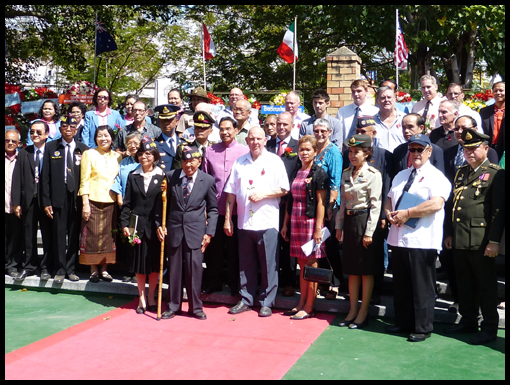 An ancient Free Thai Army veteran stands center stage surrounded by people who want tohave their picture taken with him.