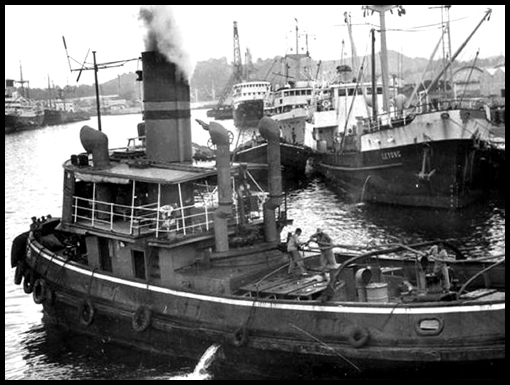 The crew of a tug in Singapore harbour haul on the hawser to tow the Empire Kittiwake from the dockside.